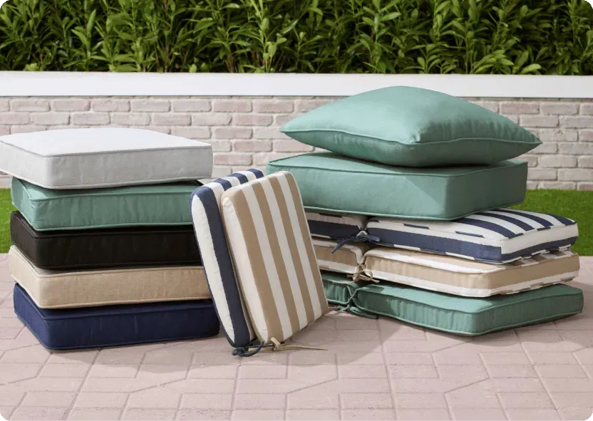 Stacked patio cushions in teal, navy, tan and striped covers, deep seat pads and back pillows with fabric ties, on a brick patio